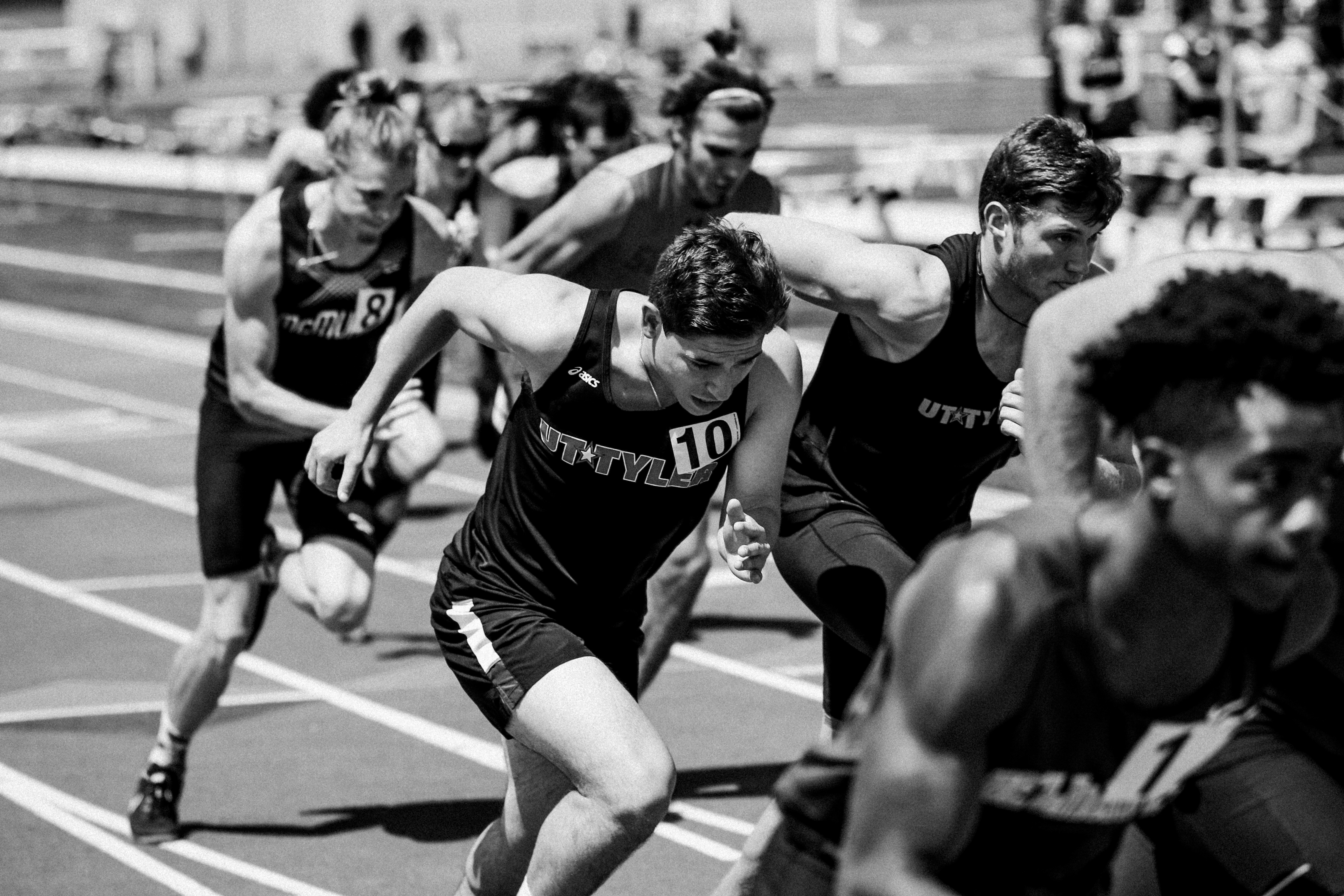 Black and white image of a group of runners on a track. 